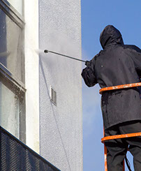 Worker high pressure spray washing side of building